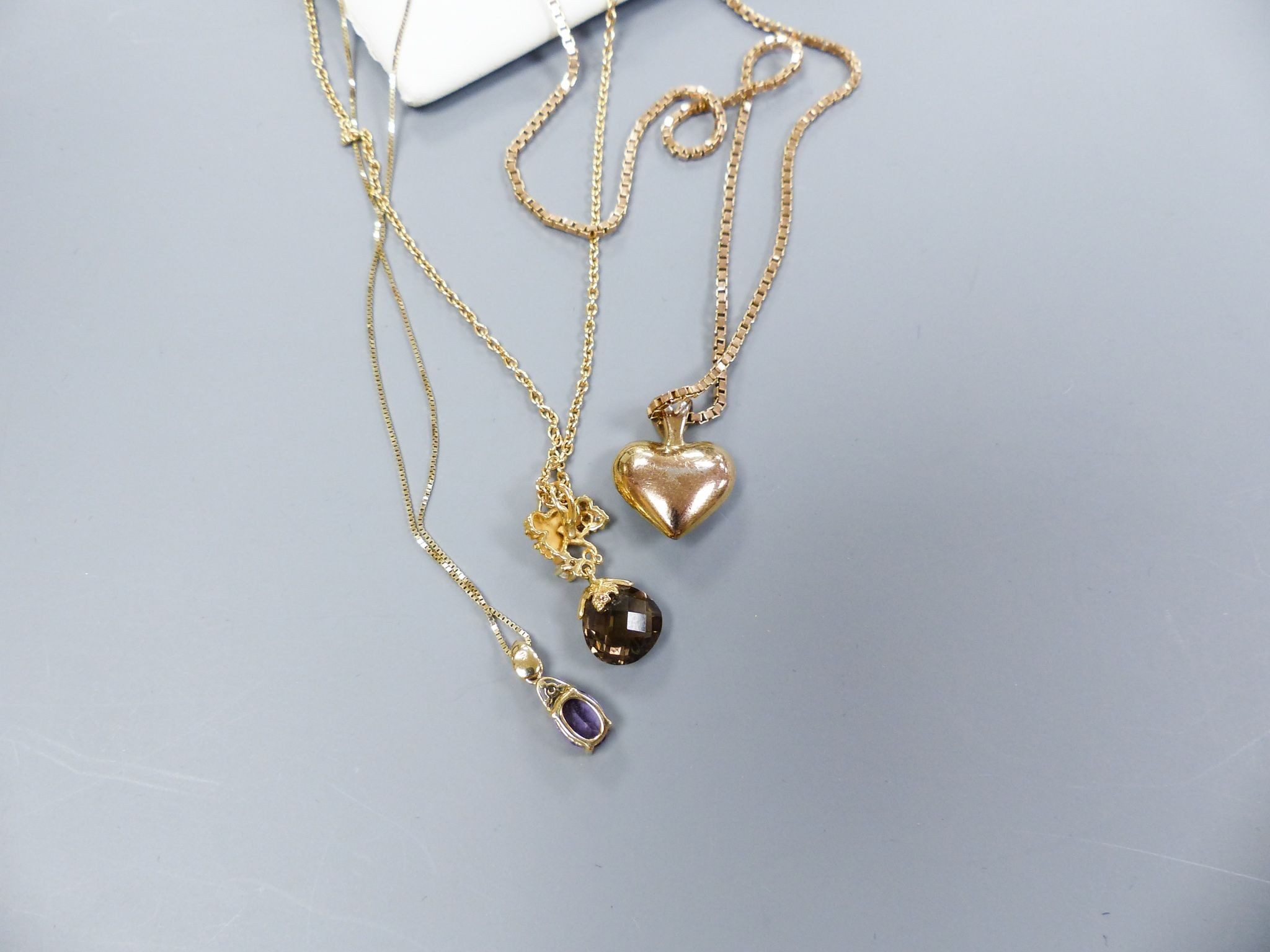 A smoky quartz pear-shaped pendant on diamond-set 'leaf' suspension and 9ct gold chain, a 9ct gold box-link chain with paste 'heart' pendant and a 9ct gold and amethyst pendant on 9ct gold fine chain.